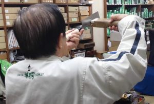 artigiano giapponese che controlla la linea della lama del coltello con un calibro di legno verificando che sia perfettamente dritta